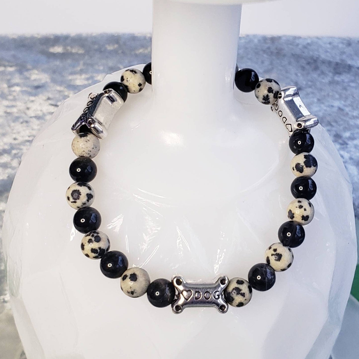 Black onyx and Dalmatian Jasper beaded stretchy bracelet with silver dog bone beads engraved with the word Dog and a heart on them displayed on an upside down white glass.