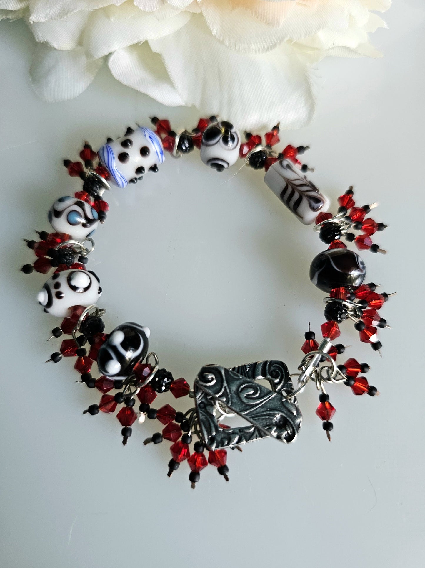 Handcrafted black and white lampwork beaded bracelet with vibrant red crystal accents. The bracelet rests on a clean white surface.