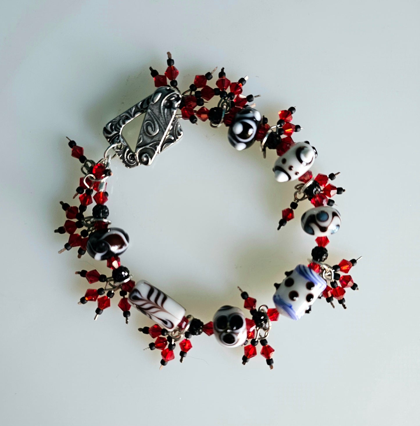 Bracelet made with black, white, and red beads, secured by a stylish silver toggle clasp. The jewelry is shown laying flat on a white surface.
