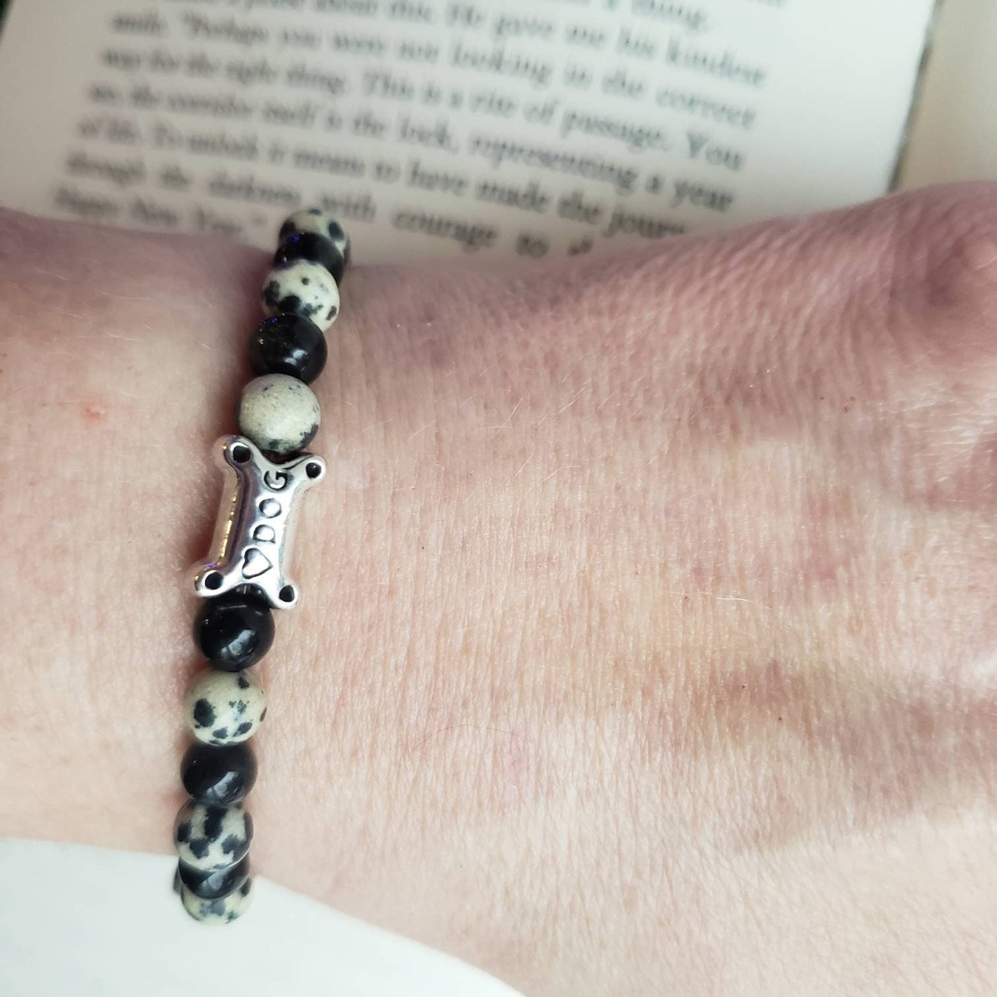 Black Onyx and Dalmatian Jasper Beaded Dog Bracelet worn on wrist to show size and look. Open book in background for staging only. 