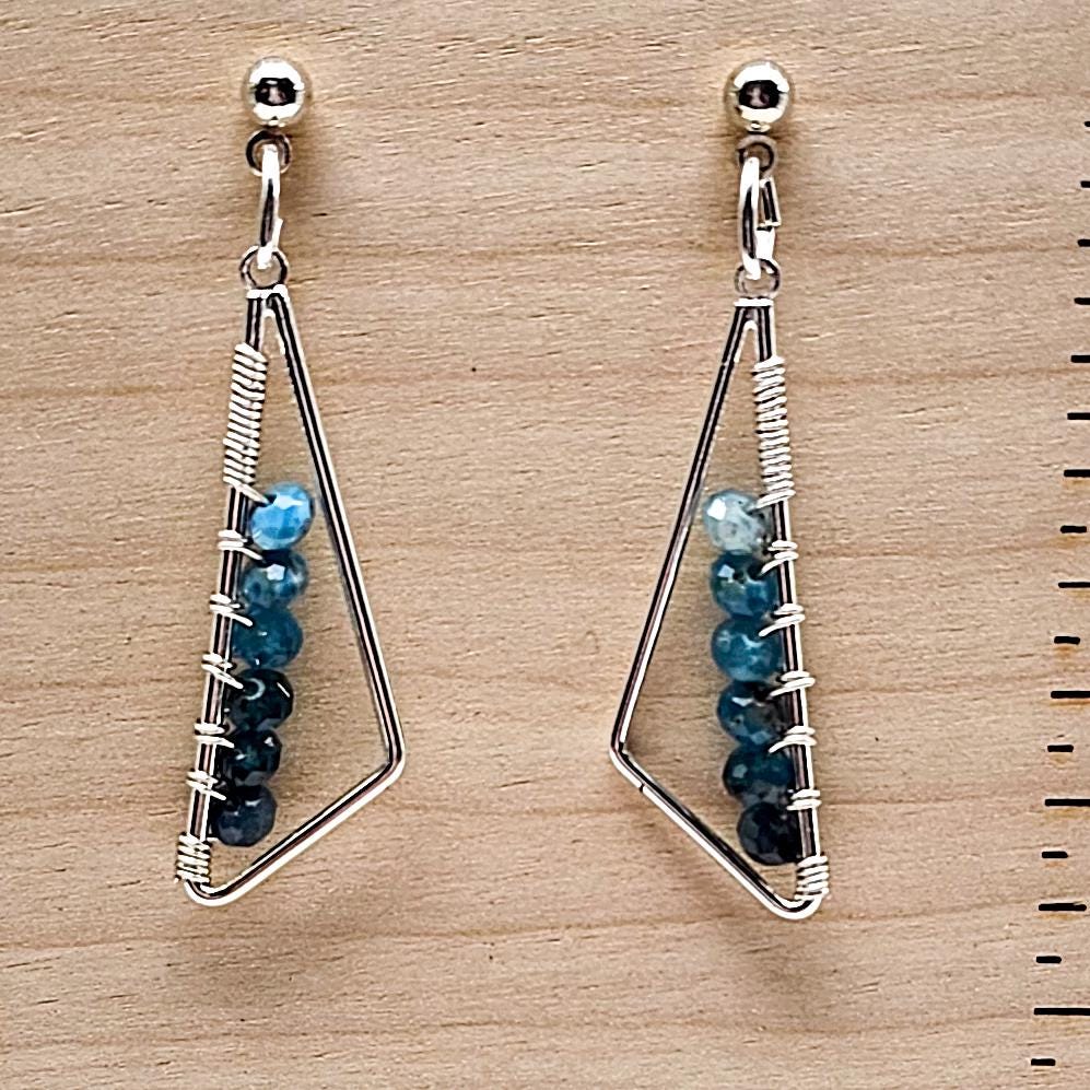 Close-up of silver and blue beaded triangle earrings displayed on a stand.