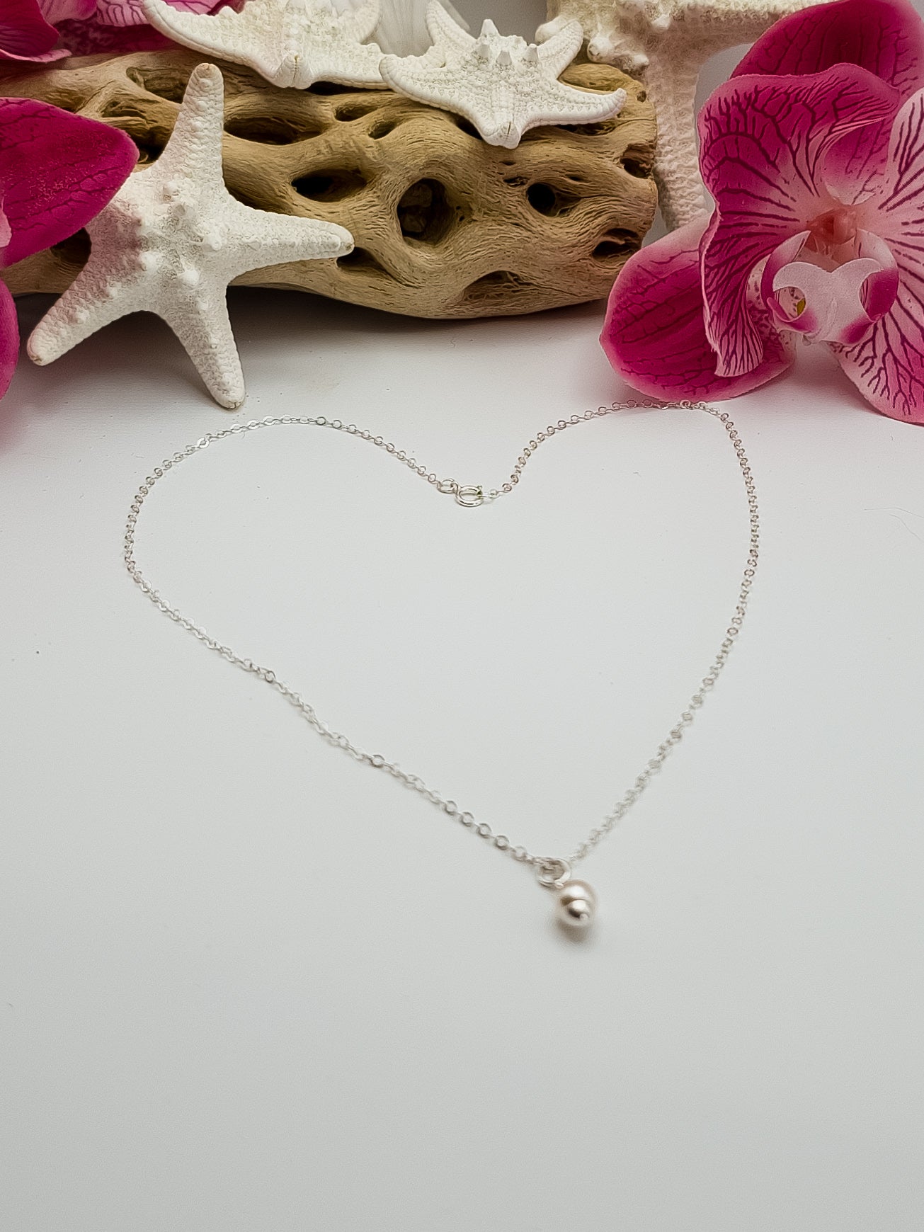 Dainty sterling silver single pearl necklace laying on a white background with beach decor in the background for staging. 