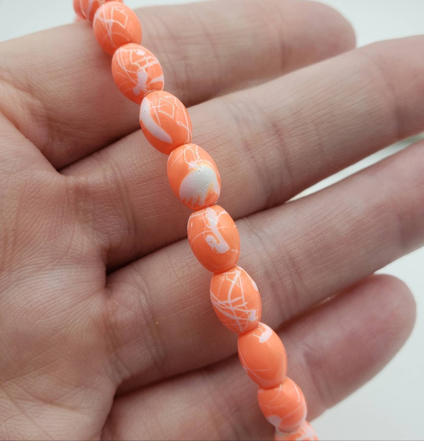 A hand gently holds a stretchy orange beaded anklet, showcasing the size of the vibrant orange beads.