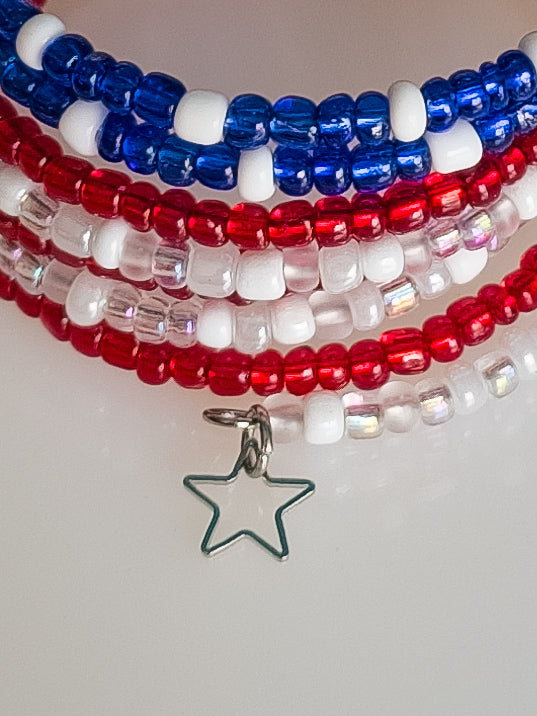 A very close view of a memory wire multi-strand bracelet featuring multiple strands of small red, white, and blue seed beads. A silver outline of a five-pointed star charm hangs prominently at the bottom.