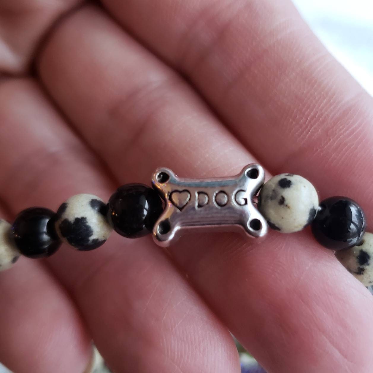 Close up of the dog bone bead showing the dog and heart engraving on the silver bead. It is being held by a hand to show the size. 