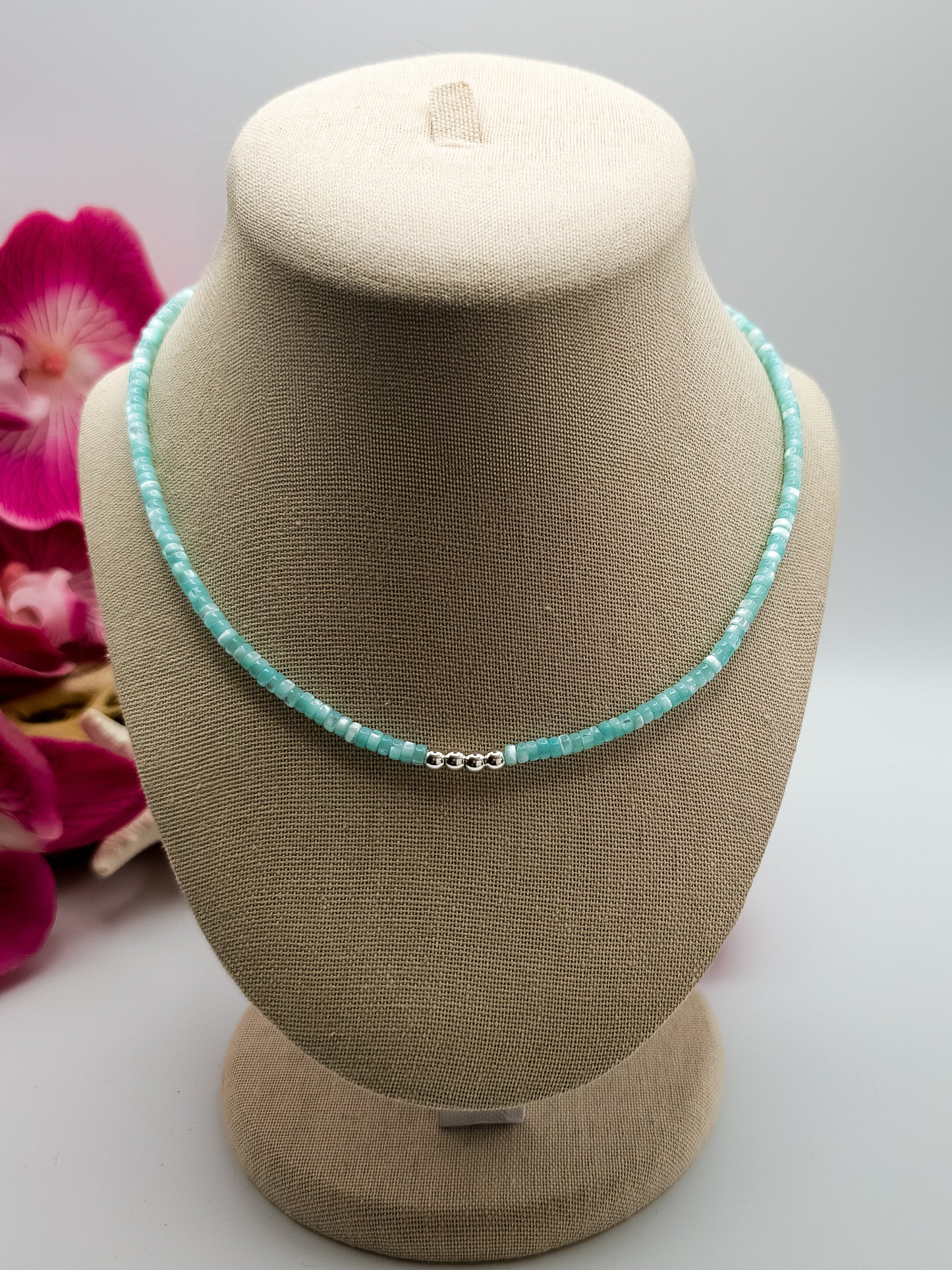 Turquoise Mother of pearl and silver beaded choker necklace with stainless steel extender chain and stainless steel lobster claw clasp on a beige neck form with flowers and driftwood background for staging. 