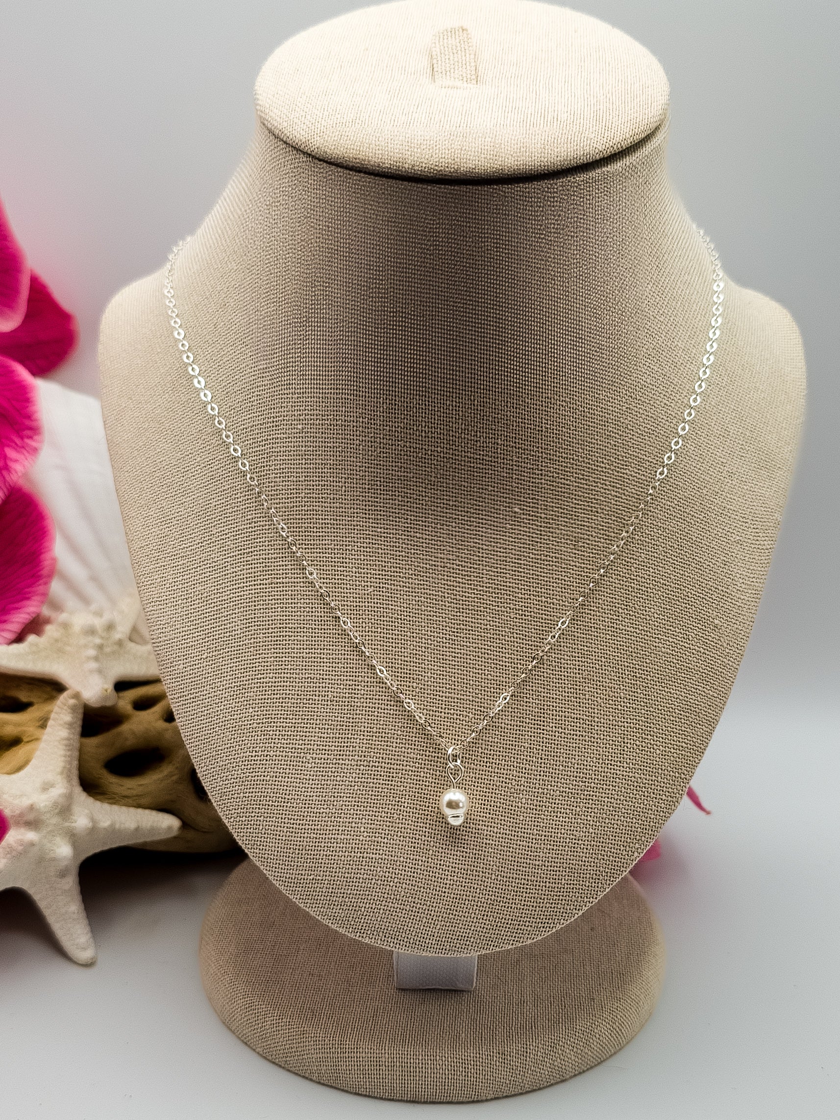 Dainty sterling silver single pearl necklace hanging on a neck display with beach decor in the background for staging. 